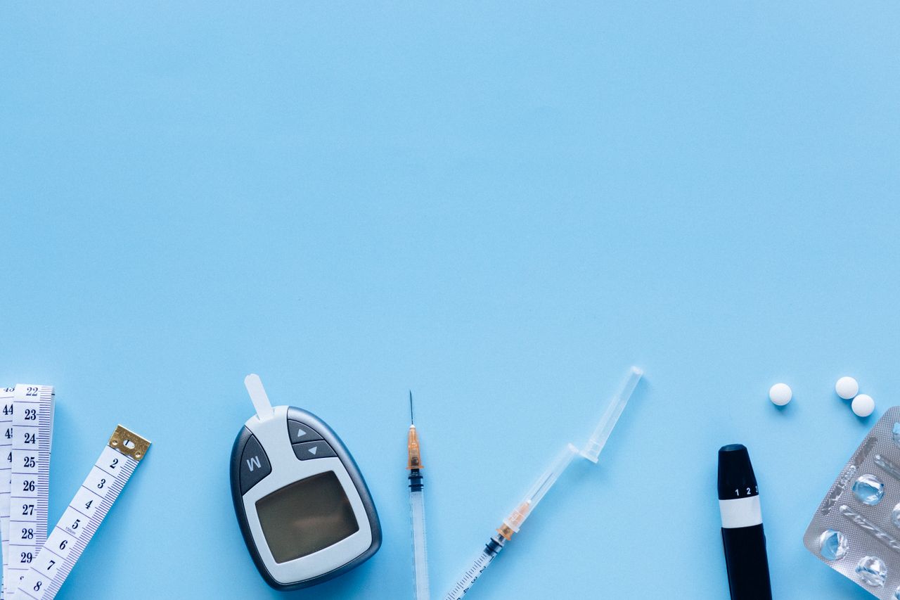 Flat lay of diabetes management tools including glucose meter, syringe, and pills on blue background.