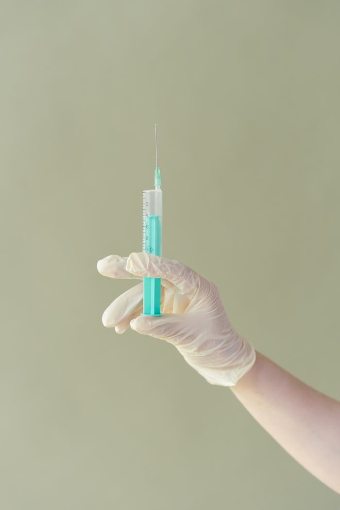 A gloved hand holding a syringe filled with blue liquid against a neutral background.